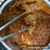Fall-Apart Instant Pot Barbacoa 9 Shredded barbacoa beef in an Instant Pot, with metal tongs on the side.