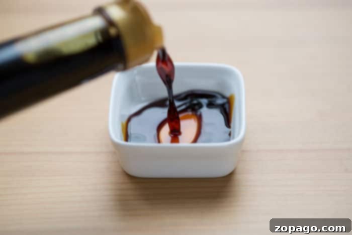 Unveiling Soy Sauce 4 A small stream of coconut aminos are like soy sauce, an ancient and savory condiment, cascades seamlessly into a pristine white dish on a wooden surface.