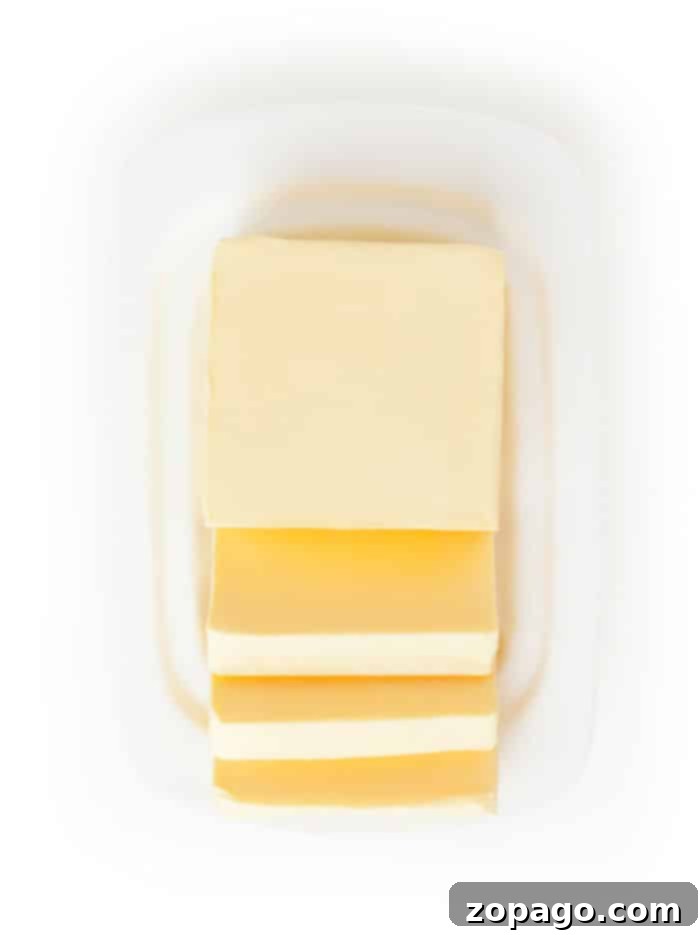 Butter Varieties Explored 2 A block of butter with four slices partially cut, showcasing different types of butter, placed on a white dish.