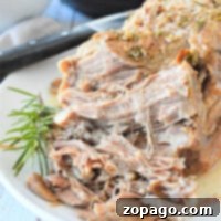 Shredded pork with herbs on a white plate, garnished with a sprig of rosemary. A frozen pork shoulder is transformed in the Instant Pot, with apples adding to the scene in the background.
