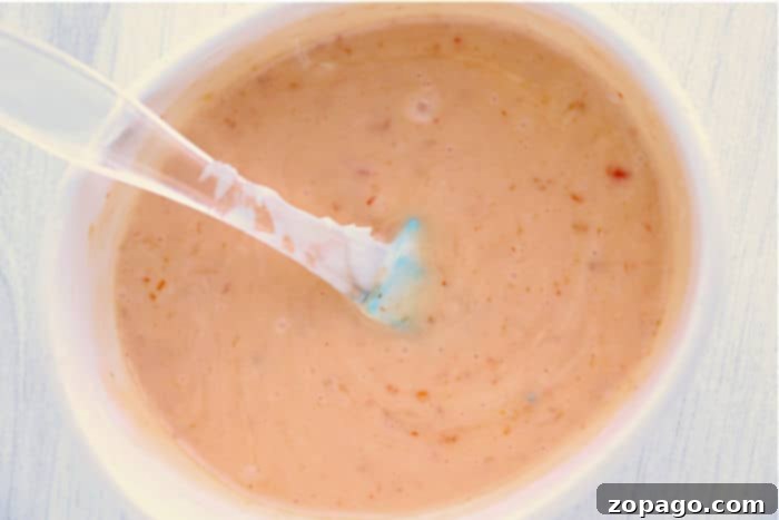 Irresistible Instant Pot Bang Bang Shrimp 5 Close-up of a creamy bang bang shrimp sauce with specks, perfect for drizzling over instant pot bang bang shrimp, served in a white bowl with a spoon.