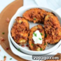 Crispy Air Fryer Potato Skins 8 A white bowl contains four air fryer potato skins with crispy cheese and bacon bits, garnished with chopped green onions. One potato skin has a dollop of sour cream.