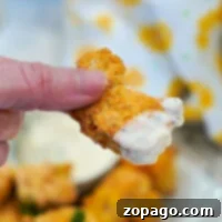 Close-up of a hand holding crispy fried fish with creamy dipping sauce.