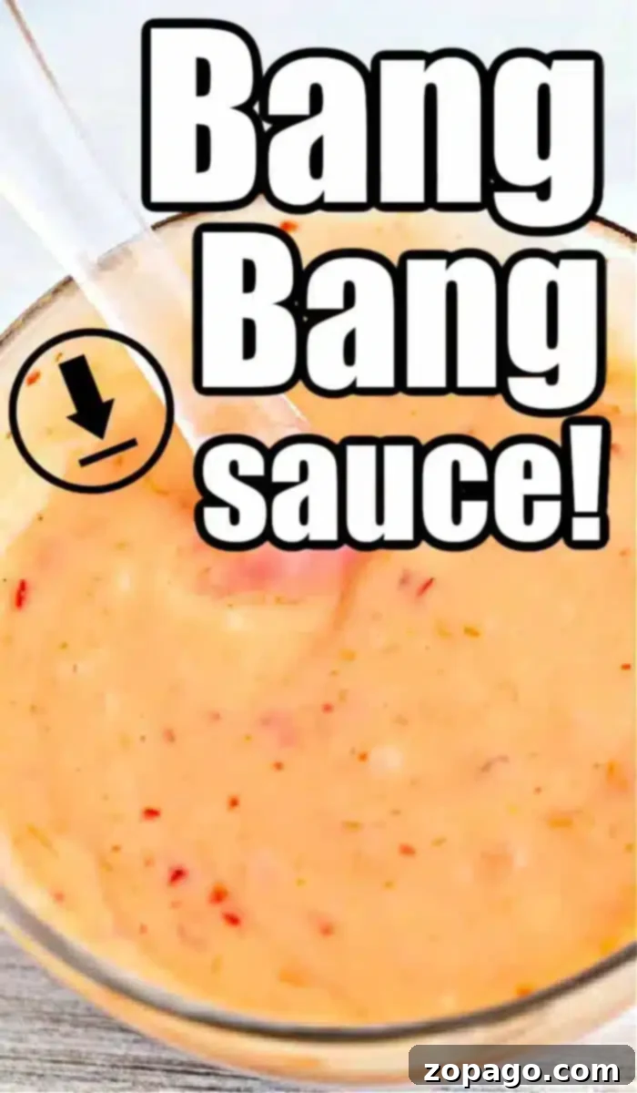 Copycat Bang Bang Shrimp Sauce 2 A close-up of a bowl filled with creamy, orange-colored bang bang shrimp sauce, sprinkled with visible red specks. A clear spoon dips into the savory mix. Bold text overlay reads, 'Bang Bang Sauce!' with a downward arrow graphic.
