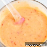 Explosive Bang Bang Shrimp Sauce 7 A glass bowl of creamy bang bang shrimp sauce with red specks and a clear spatula sits on a light surface, ready to add bold flavor to your dishes.
