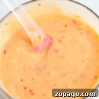 Copycat Bang Bang Shrimp Sauce 7 A glass bowl of creamy bang bang shrimp sauce with red specks and a clear spatula sits on a light surface, ready to add bold flavor to your dishes.
