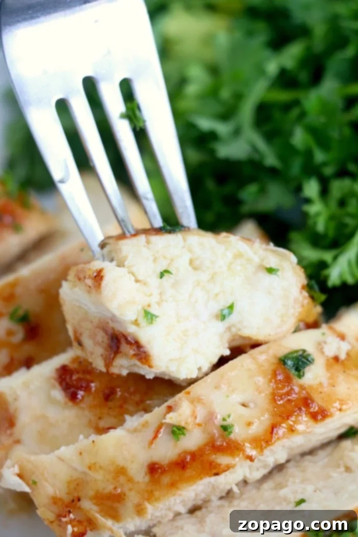 A fork holds a piece of juicy chicken breast, perfectly cooked in the Ninja Foodi, garnished with chopped herbs. The chicken is sliced with visible grill marks. Fresh green parsley or cilantro adorns the background, enhancing its visual appeal.