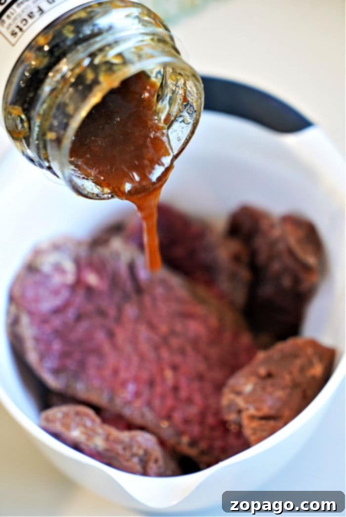 Easy Air Fryer Cube Steak 6 teriyaki sauce is being generously poured over raw cube steak in a white bowl, getting it prepped for the air fryer.
