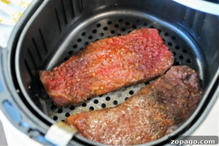 Two perfectly portioned pieces of raw cube steak resting inside an air fryer basket, patiently awaiting their transformation into a delicious meal.
