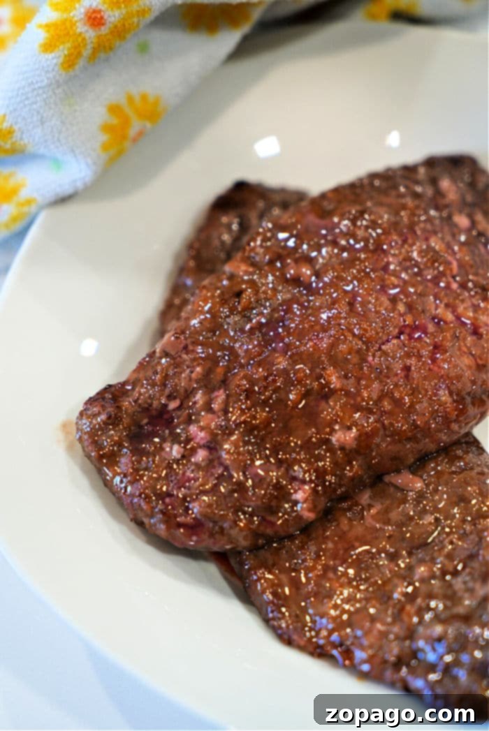 Easy Air Fryer Cube Steak 9 Close-up of raw minute steak slices on a white plate, with a patterned towel in the background, reminiscent of preparing air fryer cube steak.
