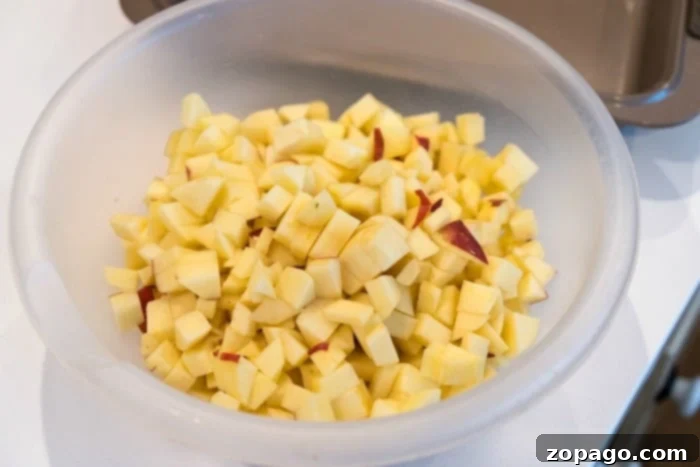 Farmhouse Apple Carrot Muffins 3 A bowl filled with diced apples rests on a white countertop, ready for baking.