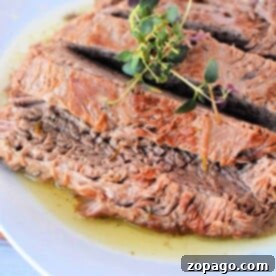 Tender Pressure Cooker Brisket 7 Sliced pressure cooker brisket with gravy on a white plate, garnished with fresh herbs.