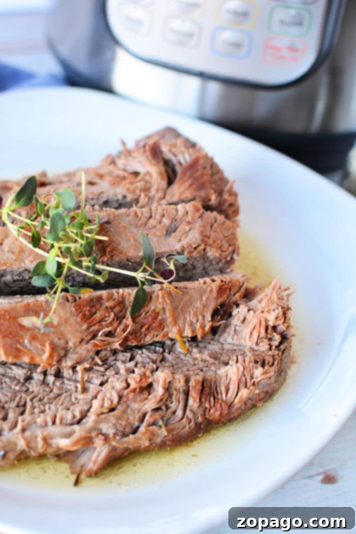Tender Pressure Cooker Brisket 8 Sliced brisket garnished with herbs on a white plate, showcasing our tender pressure cooker brisket in the background.
