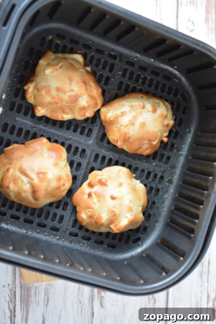 Easy Air Fryer Apple Fritters 7 Four golden-brown air fryer apple fritters neatly arranged in an air fryer basket on a wooden table, suggesting they are fresh and ready to be glazed or served.