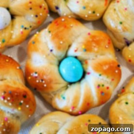 Close-up of baked brioche rolls with sprinkles, each resembling a festive Easter egg bread, topped with a blue candy egg at the center.