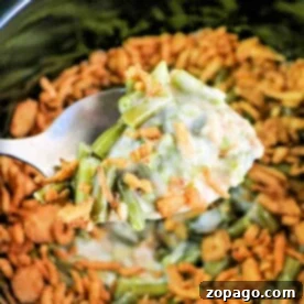 Effortless Slow Cooker Green Bean Casserole 7 A spoon gently scoops the savory slow cooker green bean casserole, capturing its rich aroma and creamy texture.
