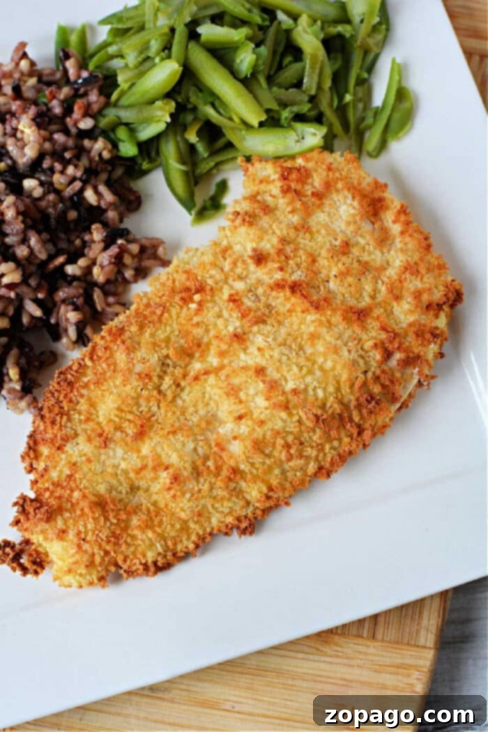 A breaded chicken cutlets sits elegantly on a plate alongside vibrant green beans and a medley of mixed rice, creating an inviting meal reminiscent of crispy chicken cutlets made effortlessly in an air fryer.