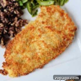 A breaded chicken cutlets sits elegantly on a plate alongside vibrant green beans and a medley of mixed rice, creating an inviting meal reminiscent of crispy chicken cutlets made effortlessly in an air fryer.