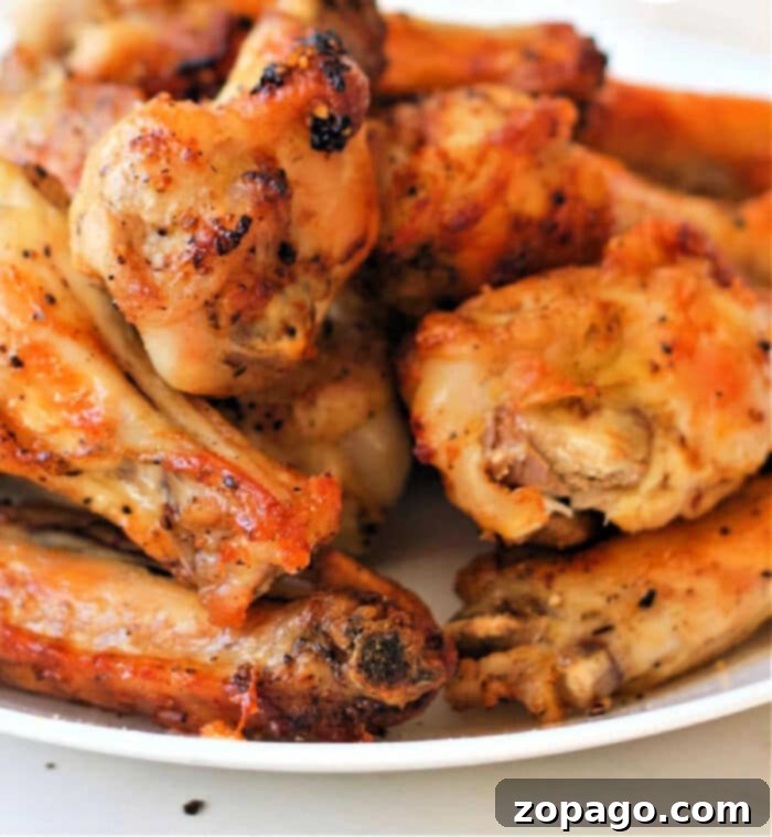 Crispy Air Fryer Lemon Pepper Wings 9 A close-up image of a plate filled with lemon pepper chicken wings, cooked to perfection in an air fryer. The wings boast a slightly charred and seasoned exterior, with a golden-brown color that adds to their appeal. The white plate enhances the presentation of this delectable dish.