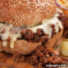 Close-up of a cheesy sloppy joe sandwich on a wooden board, with some filling spilling out and onion rings in the background, showcasing an easy sloppy joe recipe made with just 3 ingredients.