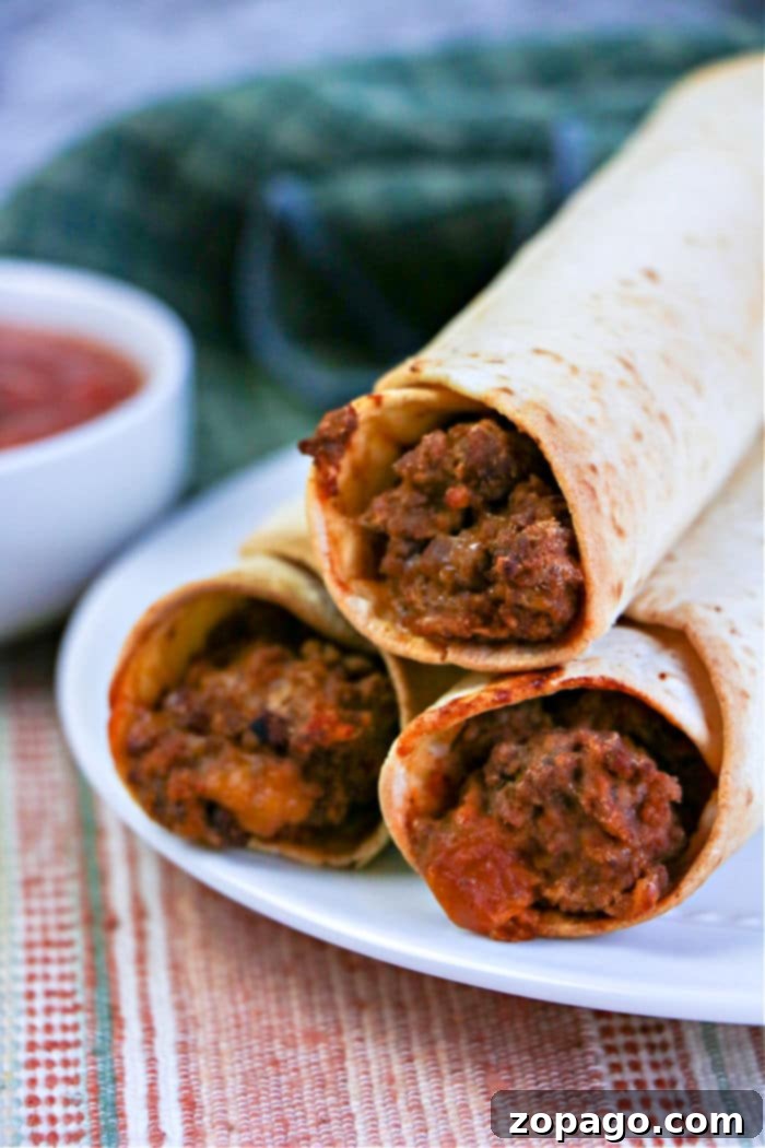 Perfectly Crispy Air Fryer Flautas 2 Three crispy air fryer flautas, rest invitingly on a white plate while a bowl of zesty salsa tempts in the background.