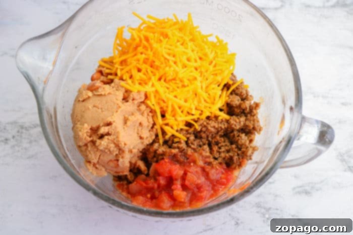 Crispy Air Fryer Flautas 5 A close-up of a bowl filled with a savory taquitos filling, a mixture of seasoned ground beef, cheese, and refried beans, ready to be rolled into tortillas.
