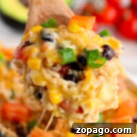 A wooden spoon holding cheesy rice with black beans, corn, bell peppers, and green onions from a savory Instant Pot Mexican chicken and rice dish.