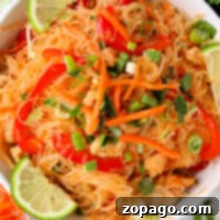 A bowl of rice noodles with chicken, carrots, bell peppers, and green onions, perfectly capturing the flavors of instant pot Pad Thai, garnished with fresh lime wedges.