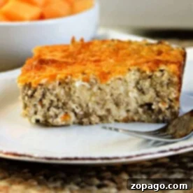 A slice of savory breakfast cheese grits casserole sits on a white plate with a fork beside it.