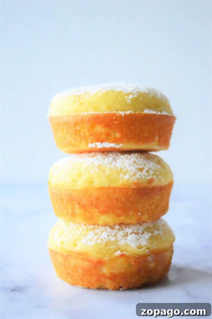 Simple & Fluffy Bisquick Muffins 2 Three stacked lemon fluffy Bisquick muffins, delicately dusted with powdered sugar, on a light background. A fresh lemon slice is visible.