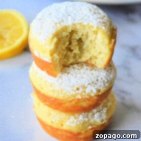 Simple & Fluffy Bisquick Muffins 10 Three lemon Bisquick muffins stacked, powdered sugar dusted on top, with a bite taken from the top muffin. A fresh lemon slice lingers in the background.
