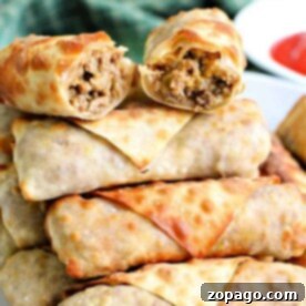 Crispy Beef Egg Rolls 8 A plate stacked with several golden-brown ground beef egg rolls. The top egg roll is halved, revealing a delicious filling of savory meat and vegetables.