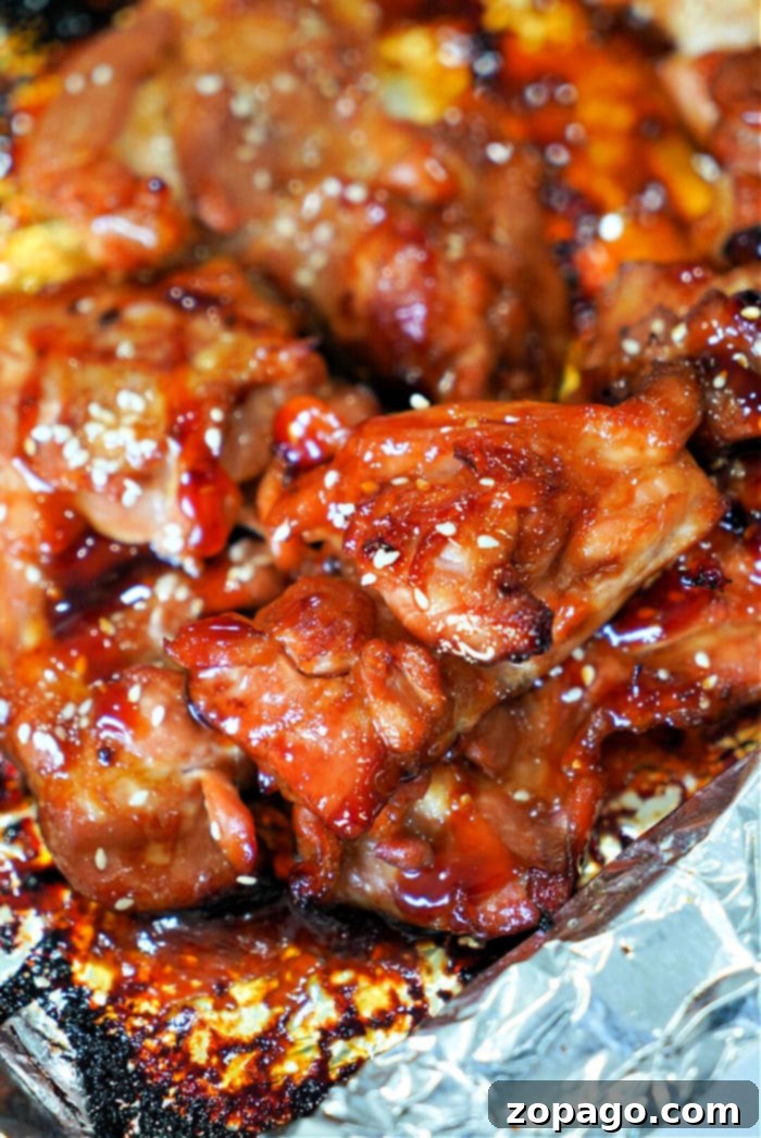 Sticky Teriyaki Chicken Thighs 2 Close-up of teriyaki glazed, baked teriyaki chicken thighs sprinkled with sesame seeds on a foil-lined tray.