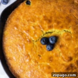 Golden cornbread baked to perfection—this Jiffy cornbread in a cast iron skillet is topped with three fresh blueberries in the center.