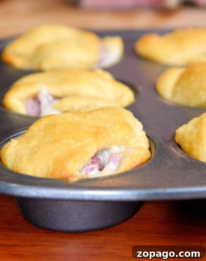 Best leftover ham recipe you will ever make and your kids will absolutely love! Use your ham leftovers after the holidays to make these crescent roll ham turnovers or rollup that a great lunch or dinner idea. Golden brown crescent roll sandwiches baked in a muffin tin, with filling visible at the edges—a perfect leftover ham recipe for easy, savory snacks.
