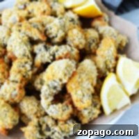 A plate of crispy air fryer oysters with lemon wedges served on brown parchment paper.
