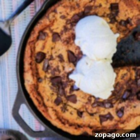 Gooey Cast Iron Skillet Chocolate Chip Cookie 8 A cast iron chocolate chip cookie topped with two scoops of vanilla ice cream sits invitingly, a serving spatula by its side.