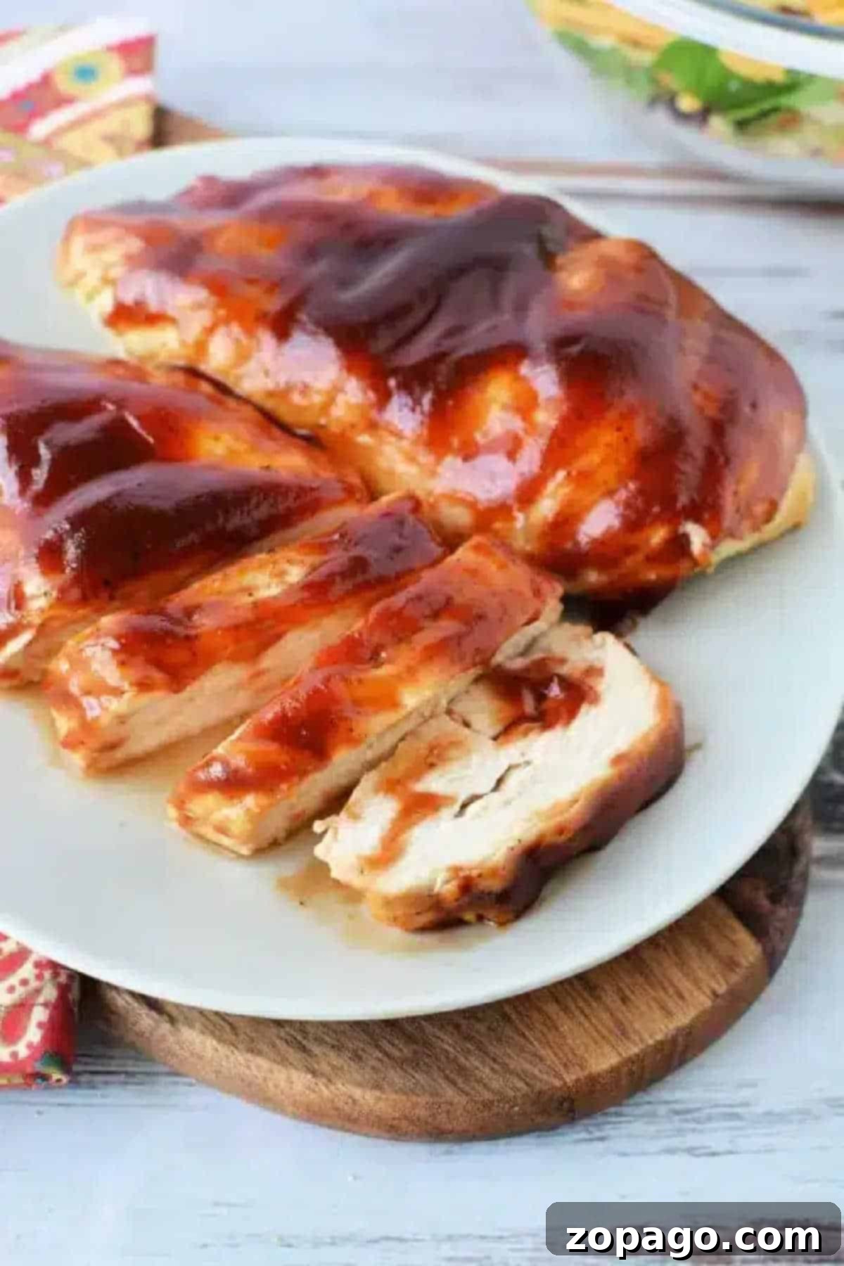 Juicy Air Fryer BBQ Chicken Breast 2 Air fryer BBQ chicken breast, sliced and coated in tangy barbecue sauce, served on a white plate atop a wooden board. A perfect healthy and quick dinner.