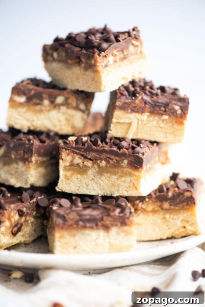 Golden Pecan Shortbread 6 A stack of chocolate and pecan shortbread bars, topped with crunchy nuts, arranged elegantly on a white plate.