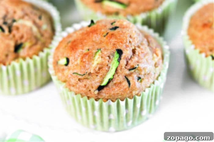 Wholesome Zucchini Applesauce Muffins 7 Close-up of applesauce zucchini muffins with a golden-brown top, nestled in a muffin pan with paper liners.