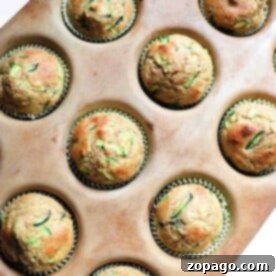 A muffin tray holds 12 freshly baked zucchini applesauce muffins, each nestled perfectly in paper liners.
