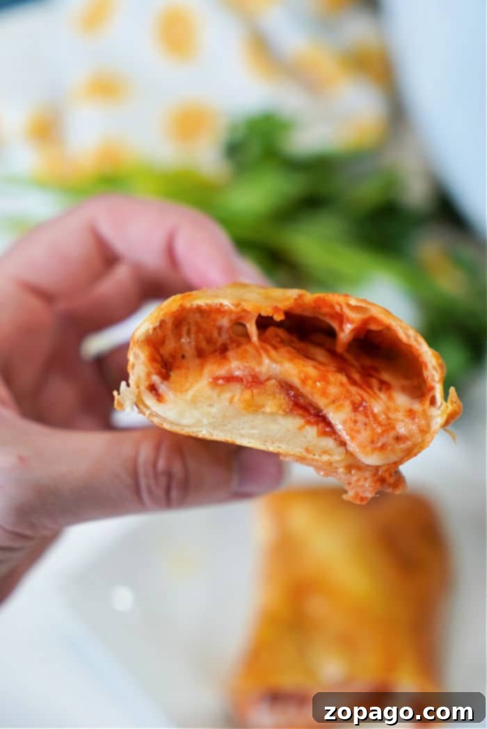 Homemade Handheld Delights 2 A hand holding a homemade pizza roll with a bite taken out reveals melted cheese and tomato sauce inside. In the background, there is a blurred green garnish on a white surface, bringing to mind freshly made hot pockets from an air fryer.