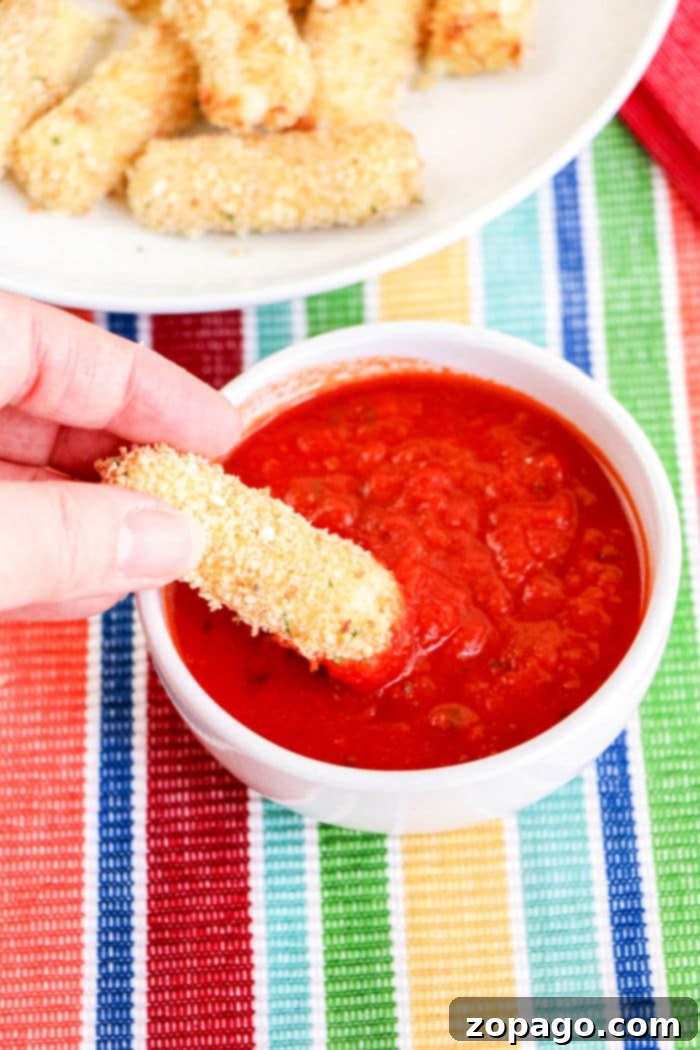 Crispy Air Fryer Mozzarella Sticks 8 A hand dipping a golden homemade mozzarella stick into marinara sauce
