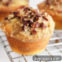 Close-up of a coffee cake muffin, boasting crumbly streusel and pecans, resting on a cooling rack.