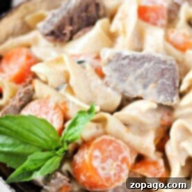 Rich & Creamy Crockpot Stroganoff 5 Savor the creamy pasta with tender beef chunks, reminiscent of a crockpot beef stroganoff, topped with carrot slices and a basil garnish in a bowl.