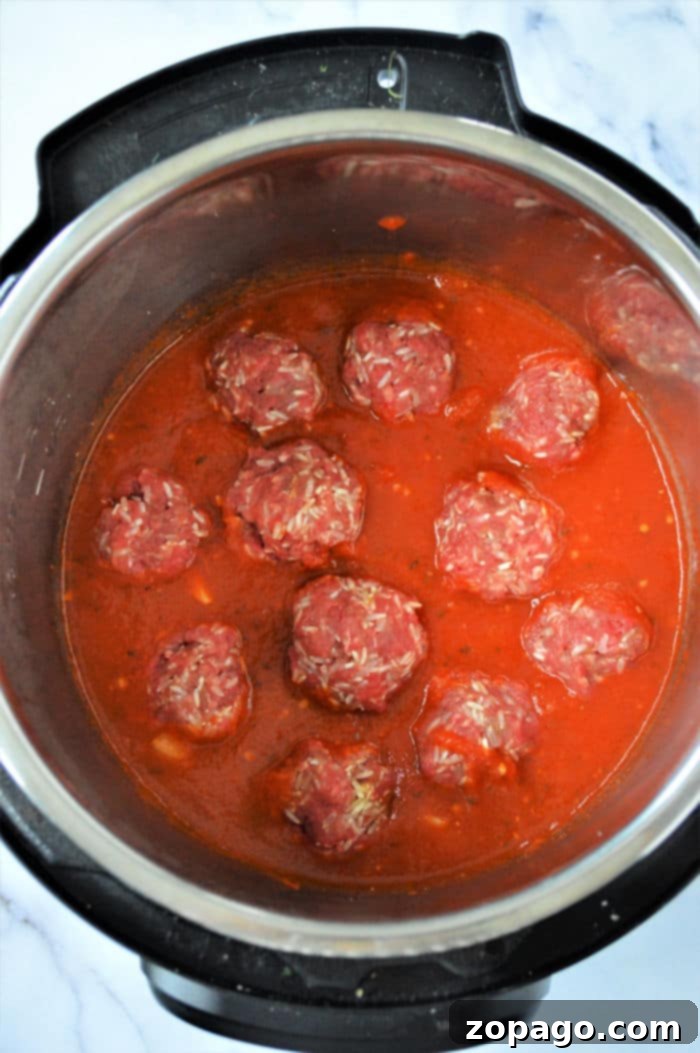 Easy Instant Pot Porcupine Meatballs 4 An instant pot filled with raw porcupine meatballs nestled in a rich red tomato sauce, ready for cooking. The cooker sits elegantly on a marble countertop.