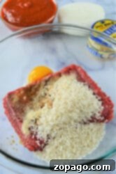 Easy Instant Pot Porcupine Meatballs 7 A glass bowl brimming with ground beef, an egg, uncooked rice, and spices sits on the countertop, ready to transform into instant pot porcupine meatballs. In the background, a bowl of red sauce accompanies an onion and a jar of minced garlic.
