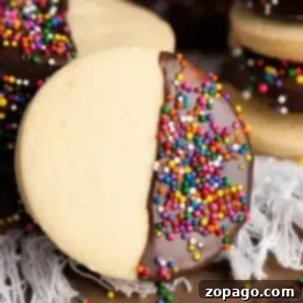 Effortless 3-Ingredient Shortbread 14 A homemade shortbread cookie, half-dipped in chocolate and adorned with colorful sprinkles, sits elegantly on a wooden table amidst an array of similar delightful treats.