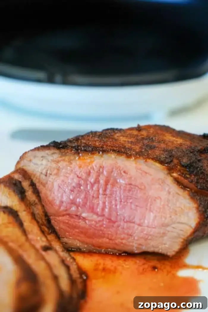 Perfect Air Fryer Tri Tip 10 Close-up of sliced, air fryer-grilled tri tip with a medium-rare center. The steak is juicy, with a charred outer layer, resting on a white surface. A small amount of juice is pooled around the slices, highlighting the meat's tenderness.