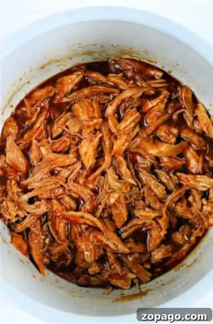 Instant Pot Pulled Pork 2 A pot filled with shredded pulled pork butt, perfectly cooked in an Instant Pot. The meat is thoroughly mixed with a rich, reddish-brown sauce, giving it a glossy appearance. Each strand of pork is evenly coated in the luscious sauce.